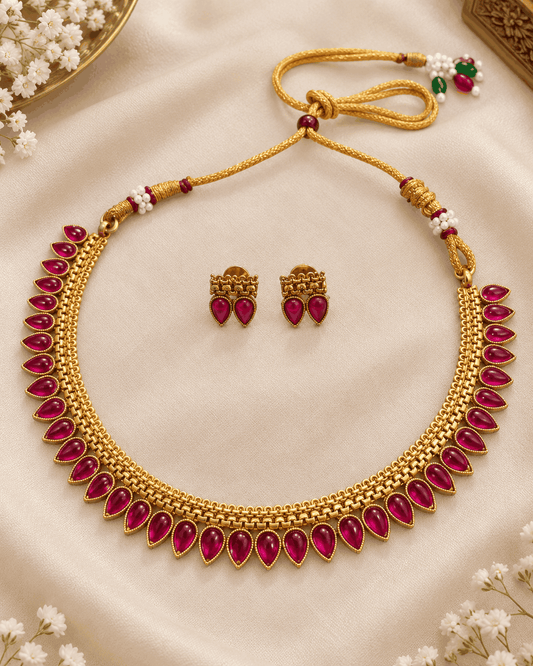 Flatlay of gold look rani pink teardrop stone necklace set with intricate chain detailing and matching earrings.