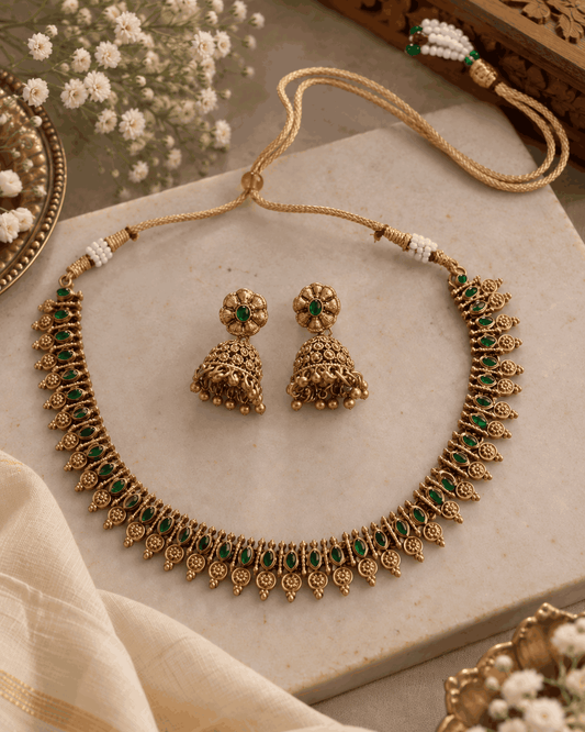 Flatlay of antique gold look necklace set featuring green stone detailing and matching traditional jhumka earrings