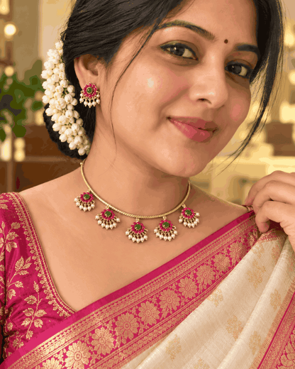 Model wearing gold look floral necklace set with pink and green stones and matching earrings