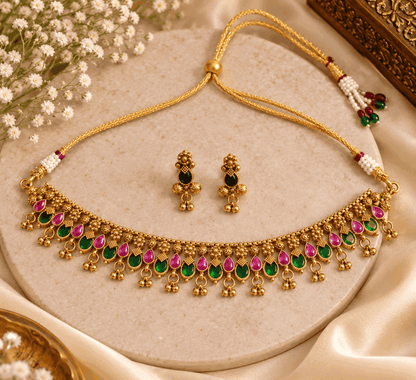Flatlay of traditional gold look choker featuring pink and green teardrop stones, ghungroo drops and matching earrings