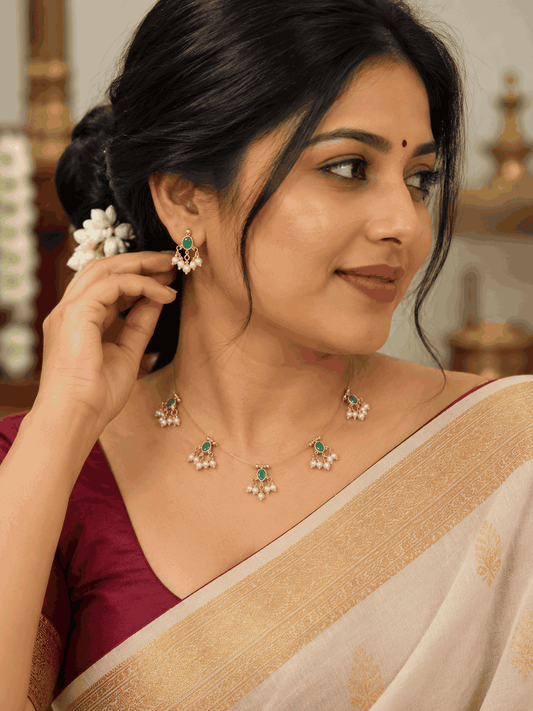 Model wearing reversible invisible chain necklace with green stone motifs, pearl-like drops and matching green earrings.